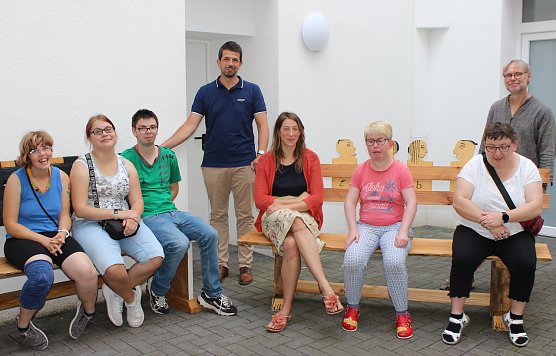 Foto: Lebenshilfe-Mitarbeiter Torsten Rieschel (4.v.l.), Praktikantin Laura Johann (5.v.l.) und Kursleiter Martin Jahn (rechts im Bild) freuen sich, die B&auml;nke an Projektteilnehmern und Hausbewohnern &uuml;bergeben zu d&uuml;rfen. Nicht alle B&auml;nkebauer waren zum Fototermin anwesend. (Foto: NTL)