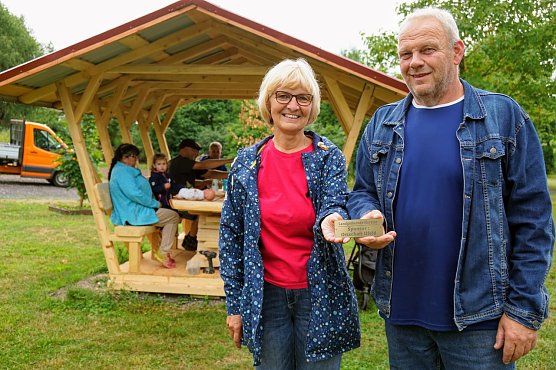 Ortschaftsb&uuml;rgermeisterin Petra Gerlach und Zimmermann Mario Eckert vor der neuen Waldschenke. Das Schild wurde an der Sitzgruppe angebracht und erinnert daran, dass der Ilfelder Ortschaftsrat diese gesponsert hat.  (Foto: Gemeinde Harztor/Susanne Schedwill)