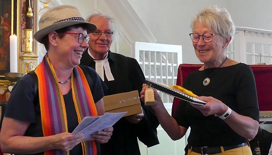 nes Delert, Gemeindep&auml;dagogin und Initiatorin des regionalen Pilgerns, &uuml;berreicht eine Fl&auml;schchen-Replik an Pilgerin Brigitte Hoppe aus Werningerode, die alle 23 Kirchen der Region besucht hat. Im Gegenzug erh&auml;lt die Gemeinde von ihr ein Fotoalbum ihrer Tour. In der Mitte Pfarrer i.R. Ehrhart Neubert. (Foto: R.Englert)