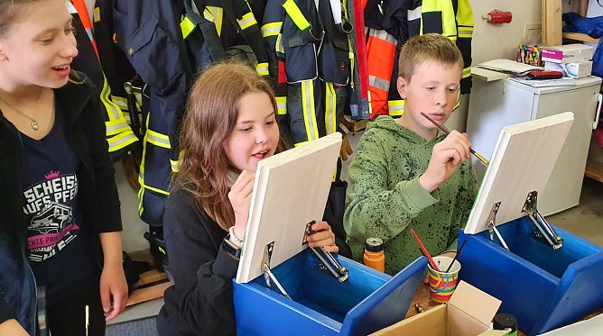 Luisa Rahn, Johanna Bernsdorf und Johann Sch&uuml;tze (v.l.n.r.) von der Jugendfeuerwehr bemalen die Klappen der Stempelk&auml;sten. (Foto: Gabriele Knust)